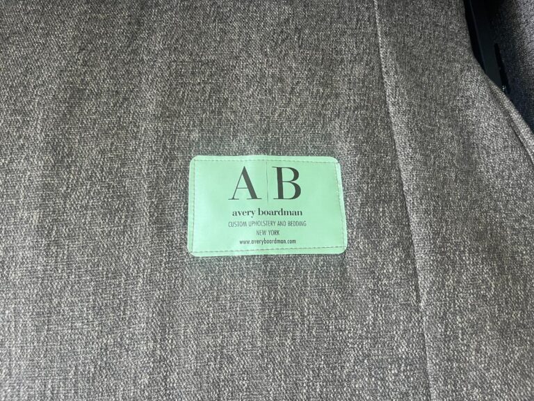 Label on grey fabric upholstery with text: "AB avery boardman custom upholstery and bedding, New York" and a website link.