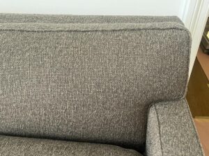 Close-up of the backrest and armrest of a gray fabric sofa, featuring a textured woven upholstery.