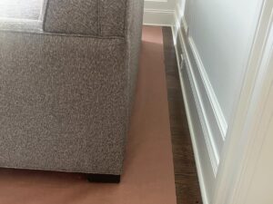 Side view of a gray upholstered couch against a white wall with brown protective covering on the floor.