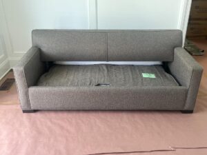 A gray upholstered sofa bed with the mattress partially extended, placed on a protective cover in a room with white walls.