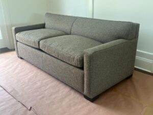 A gray upholstered sofa with clean lines and a boxy design, placed on a floor covered with protective paper.