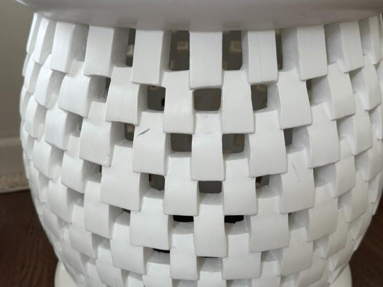 A close-up of a white, woven, textured surface resembling a basket weave design on a piece of furniture or decorative object.