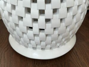 Close-up of a woven white ceramic vase with a checkered pattern, resting on a wooden surface.