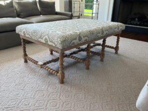 A wooden bench with intricately designed legs and a patterned upholstered cushion on a textured beige rug in a modern living room.