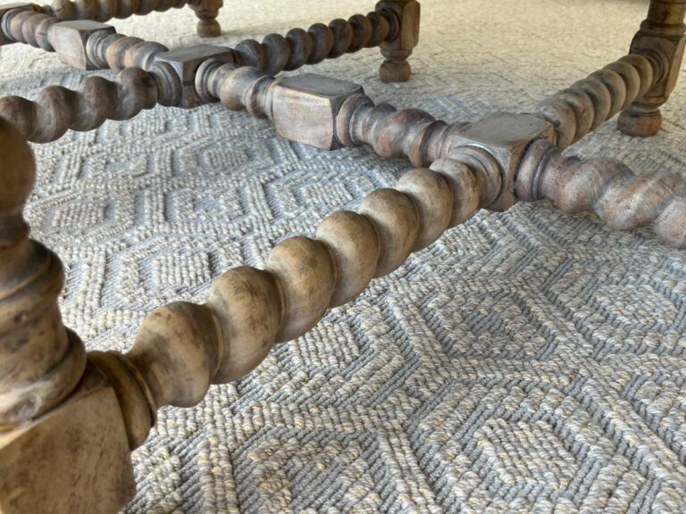 Close-up view of intricately carved wooden chair legs on a textured, patterned rug.