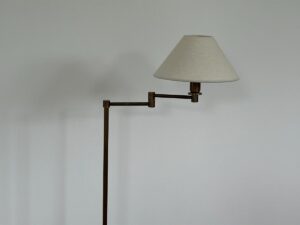 A floor lamp with a beige lampshade positioned against a plain light-colored wall.