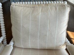 A beige cushion with white stripes placed on a wooden chair with spherical detailing on the armrests and backrest.