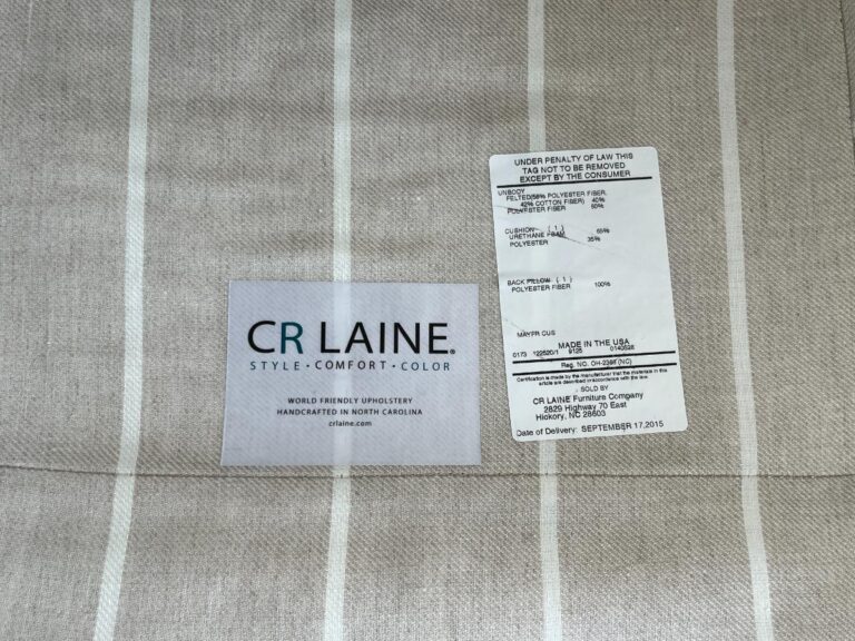 A fabric label from CR Laine indicates the product is handcrafted in North Carolina, with another tag showing a mix of polyester and down filling and legal information regarding the tag's non-removal.