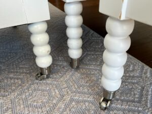 White, round, spindle table legs with caster wheels on a gray carpet.