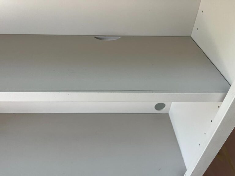 A white, empty shelving unit with three shelves. The middle shelf has a circular cutout near the back.