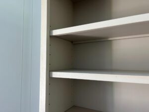 An empty white shelving unit with three shelves, attached to a light-colored wall.