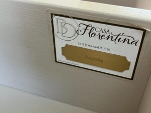 A close-up of a label on a piece of furniture that reads "Casa Florentina, Custom Made for Sophia" in gold text. The manufacturer's logo is also visible.