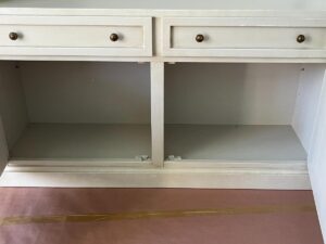 White cabinet with two drawers on top and two open compartments below, placed on a floor covered with protective paper and tape.