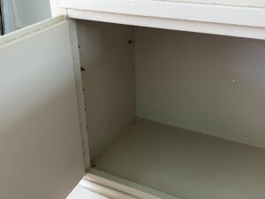 A beige cabinet with an open door reveals an empty interior and a few small marks on the inner walls.