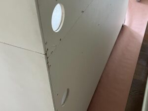 Close-up of a partially installed drywall piece with two circular cutouts, placed over a protective sheet on a wooden floor.