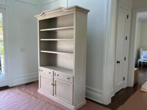 A tall, white bookcase with four shelves and two cabinets stands in a bright room with hardwood floors.
