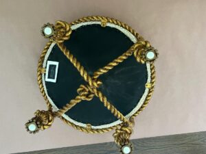 A round, dark green table with ornate gold rope-like details and four legs, viewed from above, placed on a brown surface.