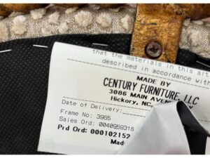 A tag affixed to furniture, showing information such as "Made by Century Furniture LLC" with an address in Hickory, NC, and other details like frame number, sales order, and product order numbers.