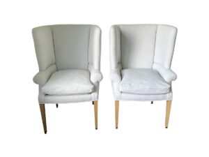 The pair of Clive Dining Chairs from Giannetti Home, featuring white upholstery, cushioned seats, and wooden legs, positioned side by side.