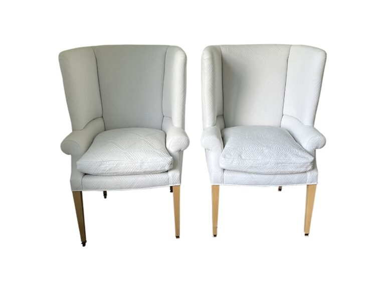 The pair of Clive Dining Chairs from Giannetti Home, featuring white upholstery, cushioned seats, and wooden legs, positioned side by side.