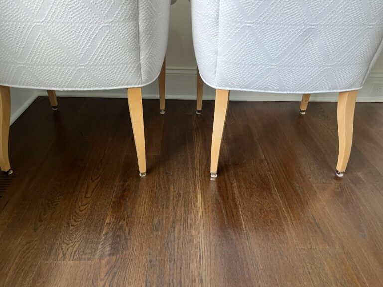 Two light-colored chairs with wooden legs placed on a dark hardwood floor.