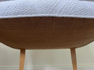 Close-up of the underside of a light-colored, upholstered chair showing wooden legs, fabric texture, and stitching details.