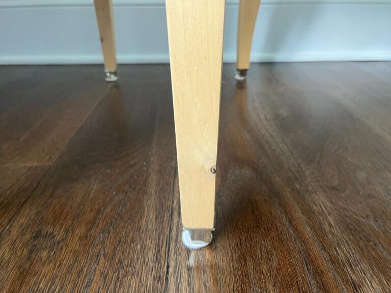 Close-up view of the leg of a wooden furniture piece, showing a protective felt pad on its bottom, placed on a polished hardwood floor.