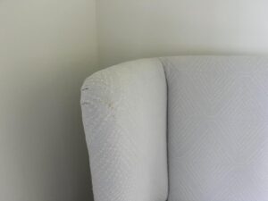 Close-up of a light gray, textured fabric on the backrest of a chair placed in the corner against a pale wall.