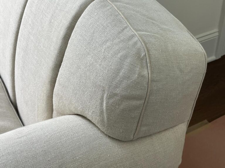 Close-up of the armrest on a light gray upholstered chair with a curved design and visible seam detailing.