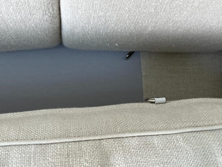 A close-up shot of a light beige fabric sofa showing the space between the back cushions and the bottom seat cushion.