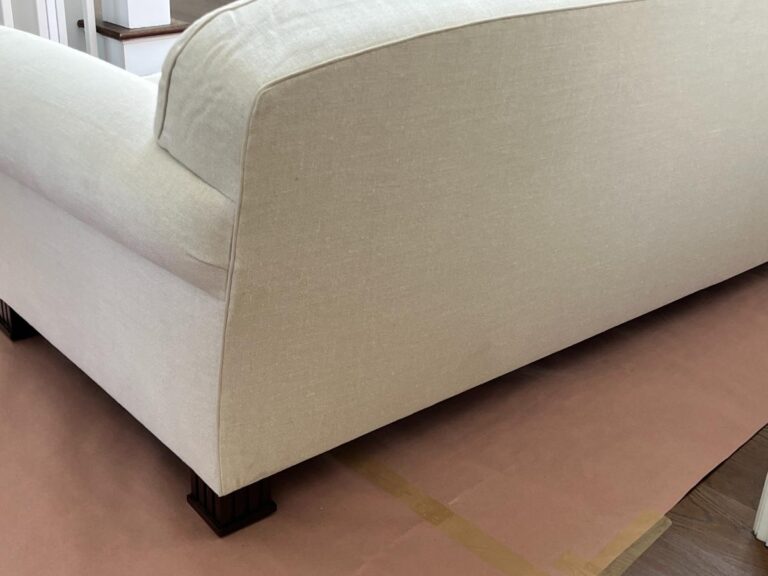 A light beige upholstered sofa is positioned on a protective brown paper covering on the floor, with dark wooden legs visible.