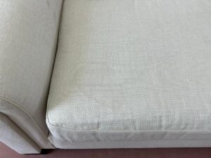 Close-up of a light gray upholstered couch, showing the corner of the seat cushion and part of the armrest.