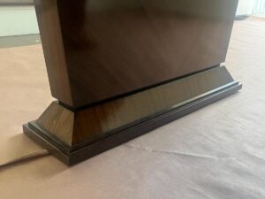 Close-up of the base of a dark wooden piece of furniture standing on a light brown surface.