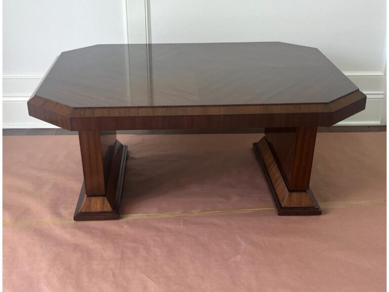 A wooden coffee table with an octagonal top and two rectangular legs sits on a light brown protective covering.