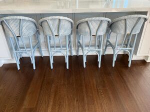 Four Kitchen Stools by Loom USA, featuring light blue seats and wicker backs, are aligned at a white kitchen island on a wooden floor.