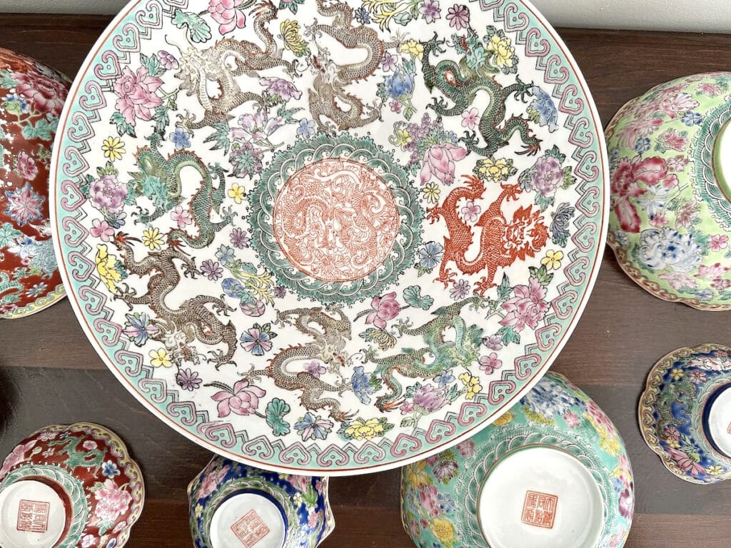 Intricately designed ceramic plate with dragon and floral patterns, surrounded by colorful, detailed vases on a wooden surface.