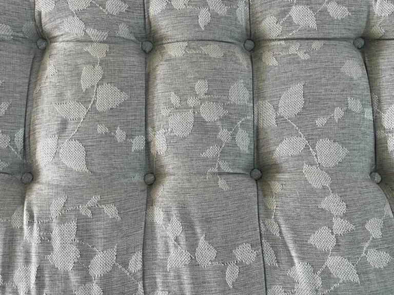 Close-up of the cushioned surface on the Zentique Louis Curve Bench in Distressed Olive Finish, showcasing a tufted design with buttons and a textured leaf pattern on light gray fabric.