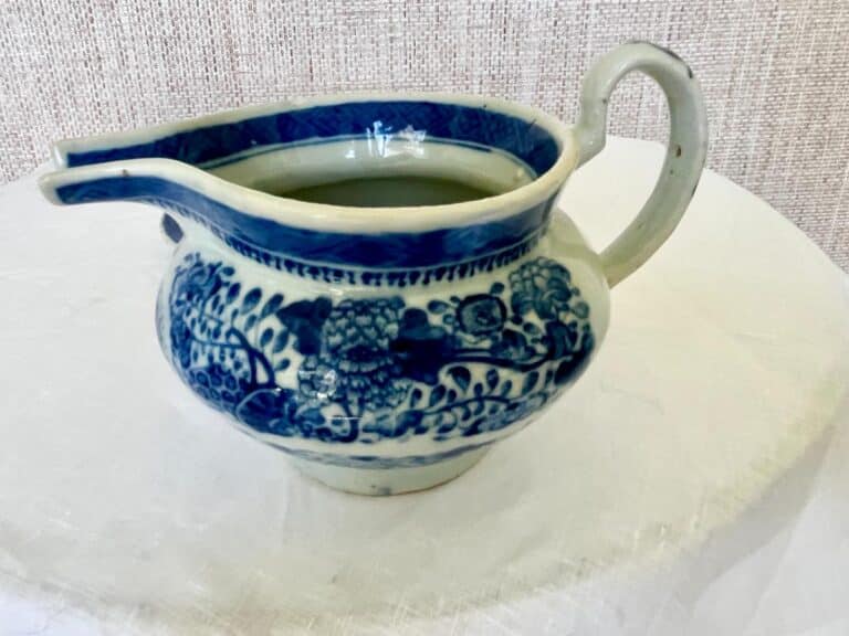 A blue and white floral-patterned ceramic pitcher with a handle sits on a white surface.