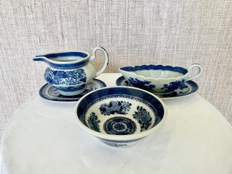 A set of blue and white ceramic dishware on a table includes a pitcher, bowl, and oval dish with floral patterns.