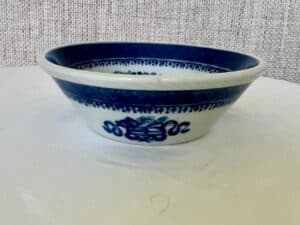 A round, white ceramic bowl with blue patterns, featuring a dragon design on the side, placed on a white surface.