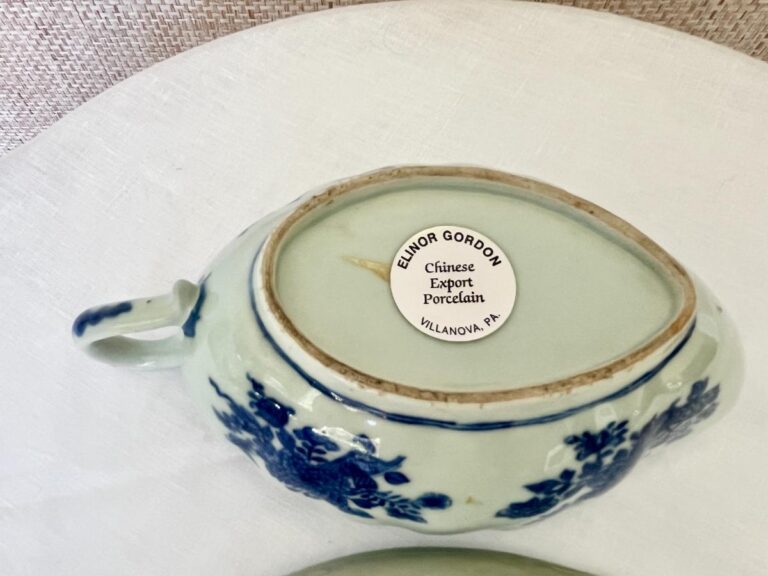 A porcelain teapot with blue floral designs and a label reading "Elinor Gordon Chinese Export Porcelain, Villanova, PA" on the lid.