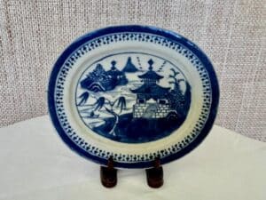 A blue and white ceramic plate with a landscape design featuring buildings, trees, and mountains on a stand.