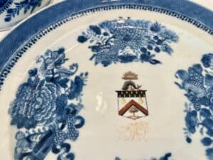 A porcelain plate with blue floral designs and a central coat of arms featuring a tree, three pears, and a zigzag pattern.