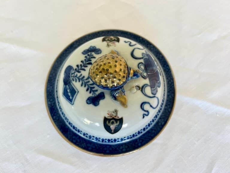 A porcelain lid decorated with blue patterns and a gold knob on a white surface.