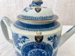 A blue and white ceramic teapot with a floral design and two crest emblems on the lid and body.