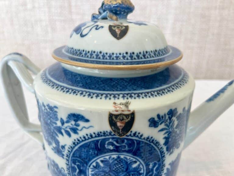 A blue and white ceramic teapot with a floral design and two crest emblems on the lid and body.