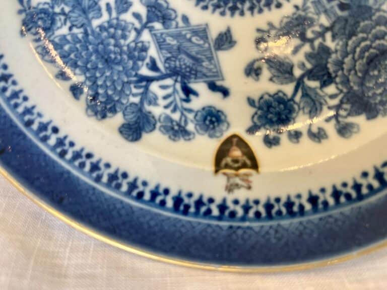 Close-up of a decorative porcelain plate featuring blue floral patterns and a small shield-like emblem on a white background.