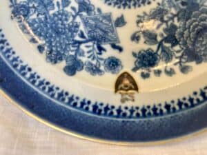 Close-up of a decorative blue and white ceramic plate with floral patterns and a small crest, placed on a white surface.