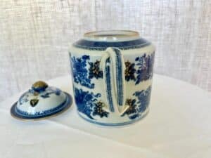 A porcelain teapot with blue floral patterns and a detached lid sits on a white cloth.