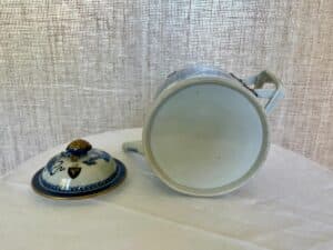 Ceramic teapot with a floral design lies on its side, with the lid placed nearby on a white surface against a textured beige background.